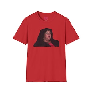 May include: A red t-shirt with a meme of a woman with dark hair and a surprised expression. The graphic is centered on the shirt, showing the woman's face and upper body. The shirt has short sleeves and a crew neck.