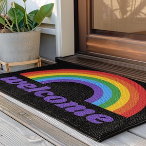 May include: A black welcome mat with a rainbow arch and the word "welcome" in purple lettering.