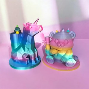 May include: Two colorful 3D-printed desk organizers. One is a unicorn with a horn and a container for pens or small items. The other is a bear holding bamboo. Both are in shades of blue, pink, yellow, and green.