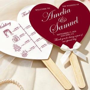 Peut inclure: Deux éventails de mariage en forme de cœur avec des manches en bois et des nœuds en ruban blanc. Un éventail est rouge foncé avec du texte blanc indiquant Welcome to the Wedding of Amelia & Samuel. L'autre est blanc avec un planning.