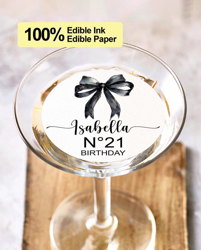K&ouml;nnte beinhalten: Ein runder, essbarer Papiersticker in Wei&szlig; mit einer schwarzen Schleife und dem Text "Isabella N&deg;21 Birthday".