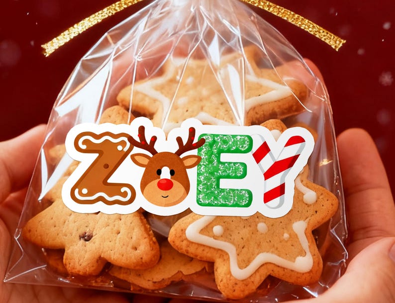 May include: A clear cellophane bag tied with a gold ribbon, filled with gingerbread cookies. The cookies are in the shapes of stars and trees, decorated with white icing. A sticker on the bag spells "ZOEY" with a gingerbread-style "Z", a reindeer, and a green "E".