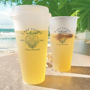 K&ouml;nnte beinhalten: Zwei durchsichtige Plastikbecher mit gelber Fl&uuml;ssigkeit. Die Becher haben ein schwarz-wei&szlig;es Design mit dem Text "Last Toast on the Coast" und einer Muschelgrafik. Der Text "Est. 2026" und "Emma's Bachelorette" sind ebenfalls auf den Bechern enthalten.