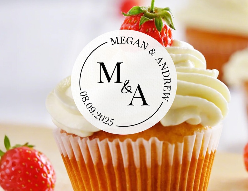 May include: White cupcake with white frosting and a round sticker that says "Megan & Andrew" with the initials "M&A" and the date "08.09.2025".