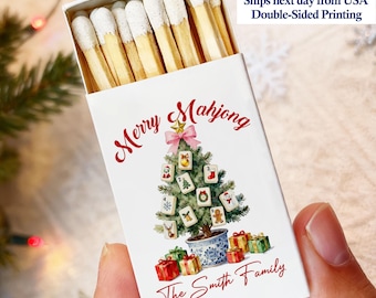 May include: A white matchbox with the words "Merry Mahjong" in red script. A Christmas tree made of Mahjong tiles is in the center. The bottom of the box reads "The Smith Family". The box is filled with matches.