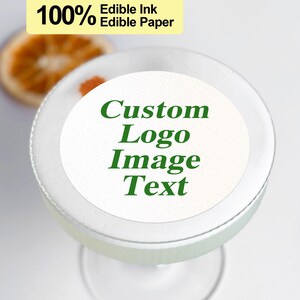 K&ouml;nnte beinhalten: Ein wei&szlig;er runder essbarer Papiersticker mit gr&uuml;nem Text, der "Custom Logo Image Text" lautet. Der Sticker befindet sich auf einem klaren Glas-Cocktailglas. Der Text "100% Edible Ink Edible Paper" ist in Gelb auf wei&szlig;em Hintergrund.