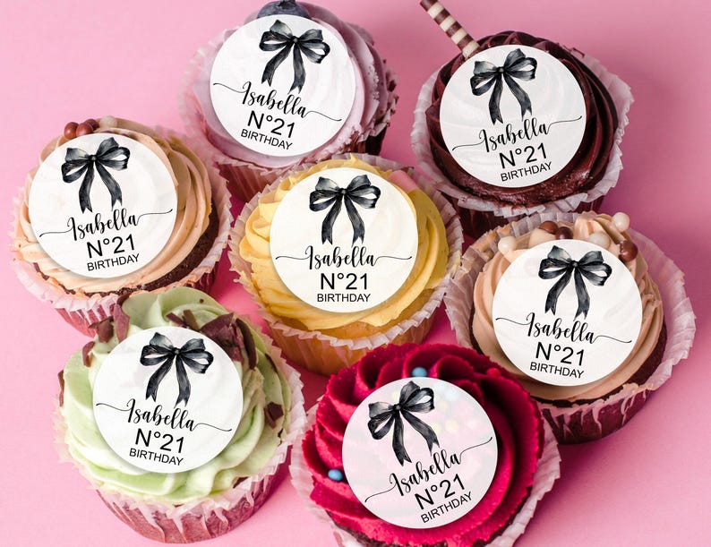 K&ouml;nnte beinhalten: Sechs Cupcakes, die mit runden essbaren Bildern verziert sind, die einen schwarzen Bogen und den Text "Isabella N&deg;21 BIRTHDAY" zeigen.
