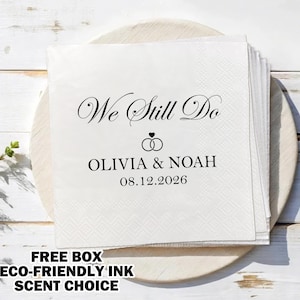 Può includere: Tovagliolo di carta bianco con testo nero che recita "We Still Do" con due anelli intrecciati e cuori sopra il testo. Sotto gli anelli e i cuori c'è il testo "OLIVIA & NOAH" e la data "08.12.2026".
