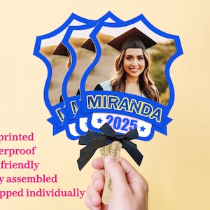 Könnte beinhalten: Ein Satz von vier blauen Fächer-Dekorationen für eine Abschlussfeier mit einem Foto eines Absolventen in Kappe und Robe. Die Fächer haben ein gelbes Sternendesign und den Text "MIRANDA 2025".
