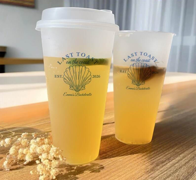 K&ouml;nnte beinhalten: Zwei durchsichtige Plastikbecher mit Deckeln, gef&uuml;llt mit einem hellgelben Getr&auml;nk. Die Becher haben ein Design mit dem Text "Last Toast on the Coast", einer Muschel und dem Text "Emma's Bachelorette" und "EST. 2026".