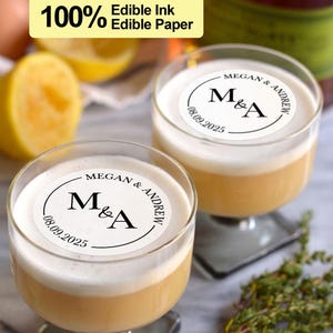 May include: Two clear glass cocktail glasses with a white edible paper topper that says "MEGAN & ANDREW" with the initials "M&A" and the date "08.09.2025".