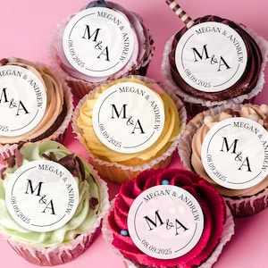 May include: Six cupcakes with white frosting and round toppers that say "Megan & Andrew" with the initials "M&A" and the date "08.09.2025".