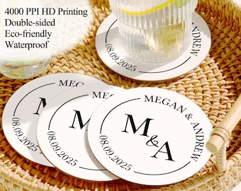 May include: Four white round coasters with black text. The coasters feature the initials "M & A" and the date "08.09.2025". The text "MEGAN & ANDREW" is also visible on one of the coasters.