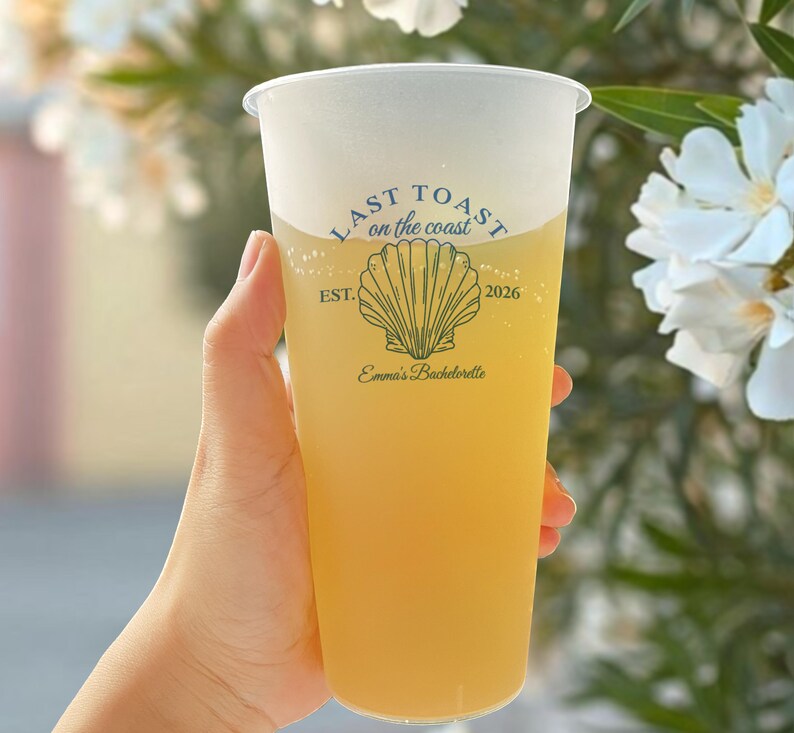 K&ouml;nnte beinhalten: Ein durchsichtiger Plastikbecher mit einem gelben Getr&auml;nk. Der Becher hat ein wei&szlig;es Design mit dem Text "Last Toast on the coast" und einer Muschelgrafik. Der Text "Est. 2026" und "Emma's Bachelorette" ist ebenfalls auf dem Becher aufgedruckt.