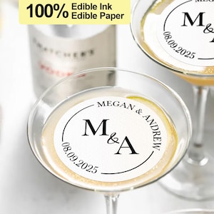 May include: Two white round edible paper drink toppers with black text. The text reads "Megan & Andrew" and "M&A" with the date "08.09.2025".