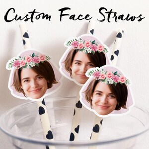 May include: Custom face straws with a woman's face wearing a floral crown. The straws are white with black heart patterns. The straws are in a clear plastic cup. The text "Custom Face Straws" is at the top.