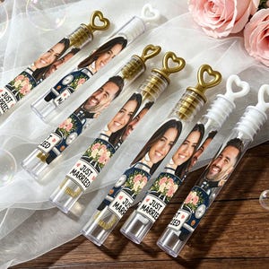May include: Six clear plastic bubble wands with heart-shaped handles. Each wand features a label with a photograph of a couple, a vintage car illustration, a floral bouquet, and the text JUST MARRIED. The wands are arranged diagonally.