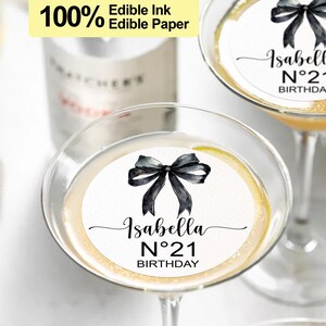 K&ouml;nnte beinhalten: Zwei runde essbare Papier-Cupcake-Topper mit einer schwarzen Schleife und dem Text "Isabella N&deg;21 Birthday".