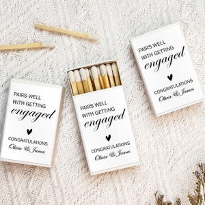 May include: Three white matchboxes with black text that reads "Pairs well with getting engaged" and "Congratulations Olivia & James".