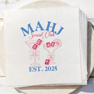 May include: A stack of white paper napkins with a blue and red design. The design includes the text "MAHJ Social Club" above two cocktail glasses with Mahjong tiles. The text "EST. 2025" is below the glasses.