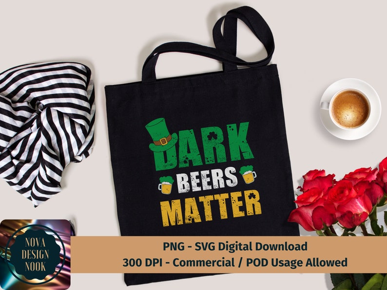 May include: A black tote bag with a green shamrock and the text "Dark Beers Matter" in a distressed font. The bag is on a white surface with a striped scarf and a cup of coffee.