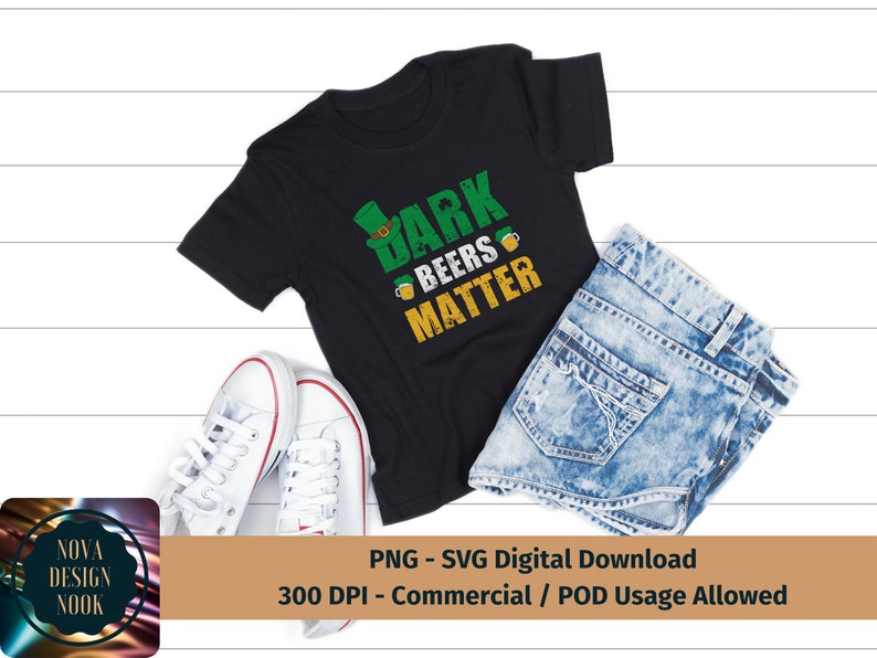 May include: A black t-shirt with a green shamrock and the text "Dark Beers Matter". The shirt is on a white wooden surface with a pair of white sneakers and a pair of blue jeans.