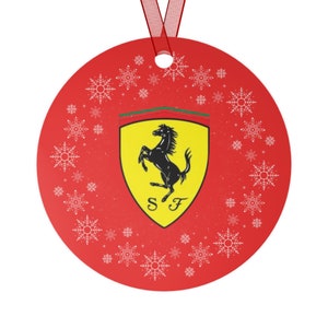 Puede incluir: Adorno navideño redondo rojo con copos de nieve blancos y el logotipo de Ferrari. El logotipo presenta un caballo negro sobre un escudo amarillo con las letras "SF". Se adjunta una cinta roja para colgar.