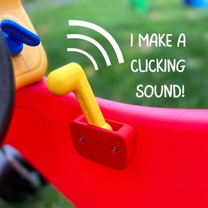 May include: A yellow plastic lever with a red plastic base. The lever is attached to a red toy car and makes a clicking sound when moved. The text "I MAKE A CLICKING SOUND!" is written in white on a white wavy line above the lever.