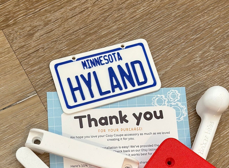 K&ouml;nnte beinhalten: Ein wei&szlig;es Plastikschild mit blauem Text, auf dem "MINNESOTA HYLAND" steht. Das Schild befindet sich auf einer Holzoberfl&auml;che mit einem Dankesschreiben und anderen Gegenst&auml;nden.