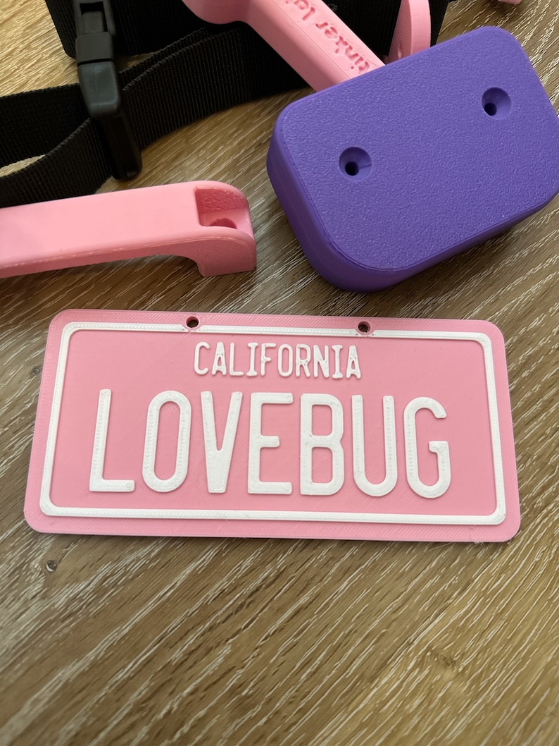 K&ouml;nnte beinhalten: Rosa Kunststoff-Kennzeichen mit wei&szlig;em Text "CALIFORNIA LOVEBUG".