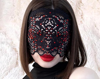 Könnte beinhalten: Schwarze Spitzen-Augenmaske mit roten Verzierungen. Die Maske hat ein zartes Blumenmuster und ist mit kleinen roten Perlen verziert. Sie bedeckt die Augen und die Stirn, mit einem gewellten Rand am unteren Rand.