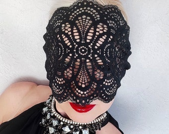 Könnte beinhalten: Eine schwarze Spitzenmaske mit einem zarten Blumenmuster bedeckt das Gesicht einer Person, die ein schwarzes Oberteil mit einer silbernen und schwarzen Strasskette trägt.