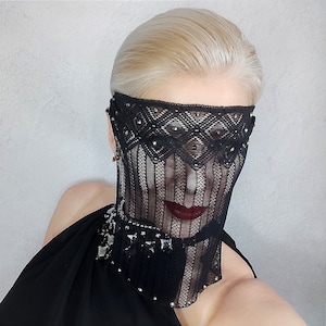 May include: A woman wearing a black lace mask with silver embellishments. The mask covers her eyes and nose, and she is wearing a black dress.
