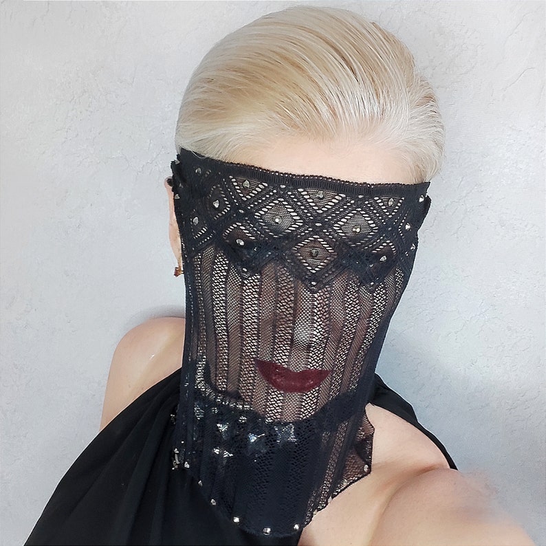 May include: A woman wearing a black lace mask with rhinestones. The mask covers her face from the forehead to the chin. The mask is made of delicate lace and has a delicate, feminine look.