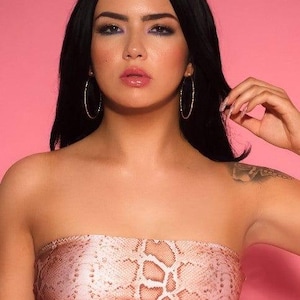 Könnte beinhalten: Ein trägerloses Tube-Top mit Schlangenmuster in Rosa- und Brauntönen. Die Person trägt goldene Creolen. Der Hintergrund ist einfarbig rosa.