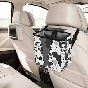 May include: A car trash bag with a black and white splatter pattern. The bag is rectangular and hangs from the headrest of a car seat. The interior of the bag is gray, and the top edge is black.