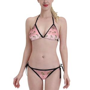 Könnte beinhalten: Rosa-weißer Bikini mit Palmenprint. Das Bikinioberteil ist im Dreieckstil mit verstellbaren Trägern. Das Bikiniunterteil ist im Binde-Stil.