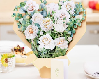 May include: A bouquet of white roses and greenery in a brown paper wrapper with a small card that says "A Fall of Roses".