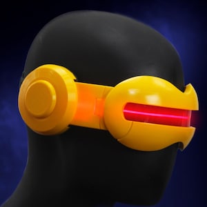 Puede incluir: Una visera de color amarillo brillante con una franja de luz roja horizontal en el centro. Las gafas cuentan con paneles laterales circulares y un diseño de marco liso y curvo que envuelve la cabeza, creando un aspecto audaz y futurista.
