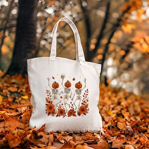 Natural cream canvas tote bag showcasing the Wildflower Skeleton design among autumn leaves and botanical skeleton details.