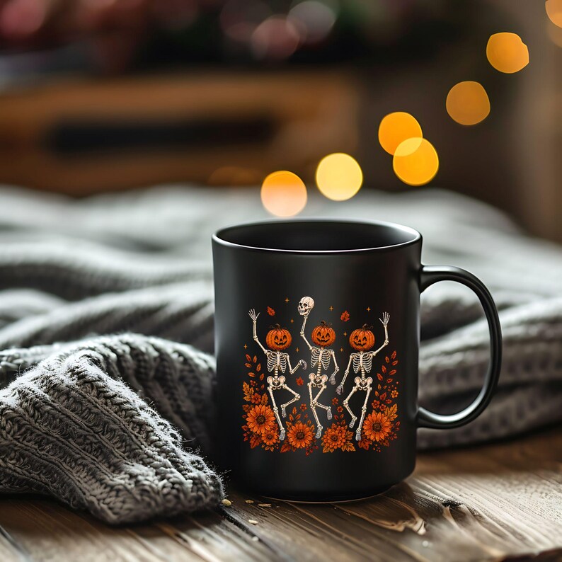 Matte black ceramic mug featuring the Wildflower Skeleton artwork with orange flowers and a cute spooky skeleton theme.