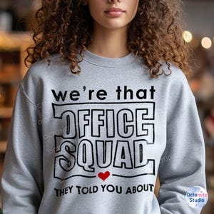Curly-haired woman wears That Front Office Squad sweatshirt with bold heart detail – awesome for coworker appreciation or leadership quotes gift themes. Works well on hoodies, mugs, and planners.