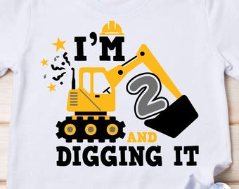 May include: A yellow and black excavator with a gray number 2 in the bucket. The text "I'm 2 and digging it" is written below the excavator. This is a digital design for a t-shirt.