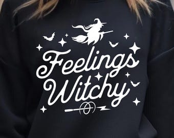 Puede incluir: Sudadera negra con un gráfico blanco que dice "Feelings Witchy". El diseño incluye una bruja en una escoba, murciélagos, estrellas y una varita mágica. La parte inferior de la imagen tiene el texto "SVG - DXF - PNG - EPS".
