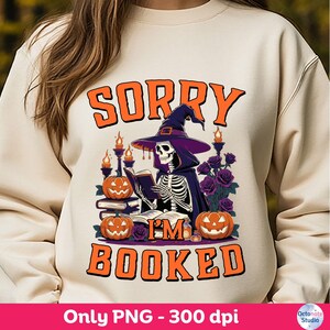 Peut inclure: Sweat-shirt crème avec un motif sur le thème d'Halloween. Le motif représente un squelette portant un chapeau de sorcière et une cape, lisant un livre, entouré de citrouilles et de roses. Le texte dit "SORRY I'M BOOKED" en orange.