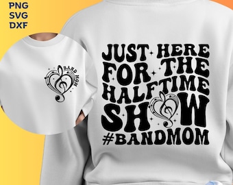 Op de afbeelding: Witte trui met zwarte tekst die "Just Here For The Halftime Show #BandMom" luidt. Een klein zwart-wit muzieknootontwerp bevindt zich rechtsonder in de tekst.