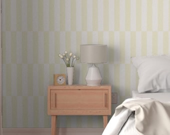 May include: Wallpaper featuring a repeating vertical pattern of alternating pale yellow and white rectangular blocks. The design covers the wall behind a wooden nightstand, a lamp, a small clock, a vase with flowers, and a bed with white bedding.