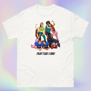 Puede incluir: Camiseta blanca con un gráfico de un grupo de personas posando en formación piramidal. El texto "FIGHT CLUB (1999)" está impreso debajo de la imagen.