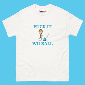 May include: White t-shirt with the text "FUCK IT WII BALL" in blue. The graphic features a cartoon character bowling with a blue and white ball. The shirt has a small "BAD + ATTIRE" logo near the collar.
