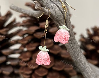 May include: A pair of pink and green crocheted flower earrings with gold hooks. The earrings are hanging from a branch.